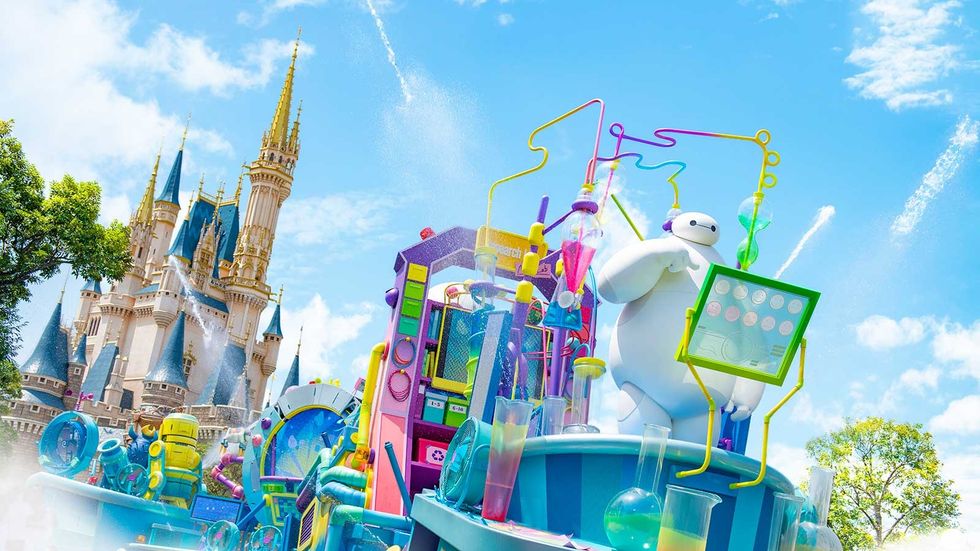 Colorful parade float with a white robot near a fairytale castle under a blue sky.