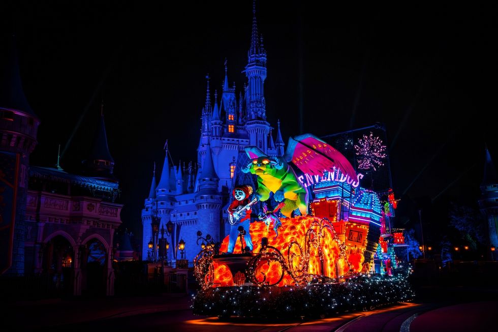 Colorful parade float with characters in front of a lit castle at night.
