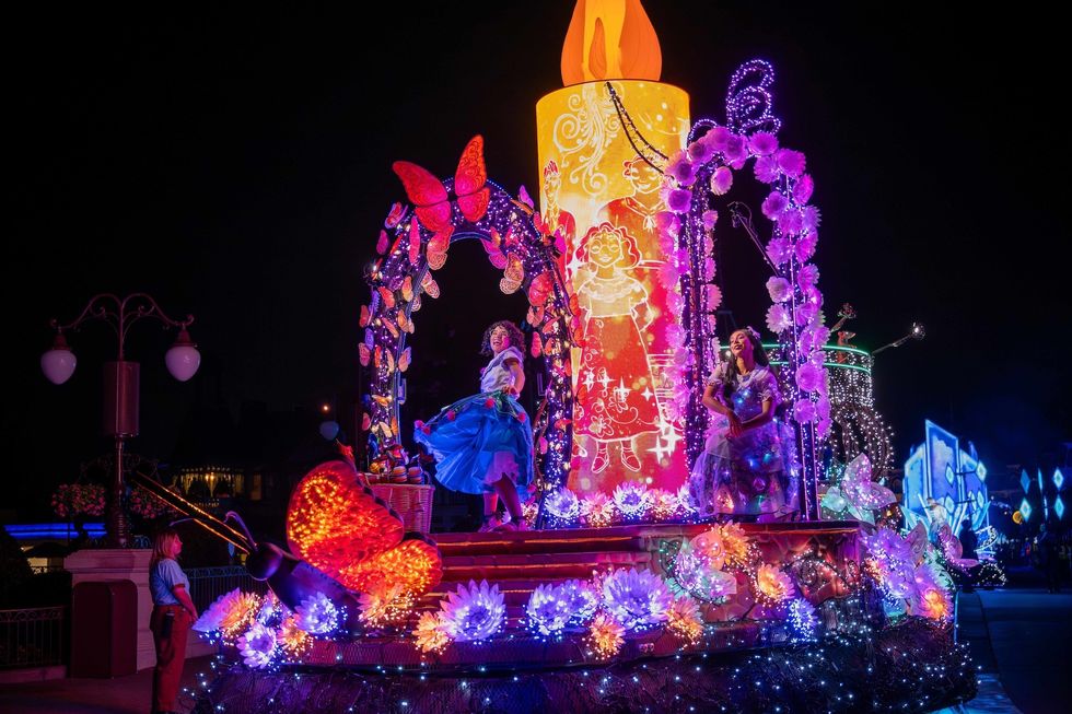 Colorful parade float with performers and large candle decoration at night.