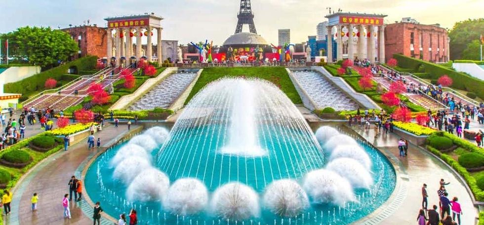 Colorful park with fountain, steps, and replica monuments, bustling with visitors.