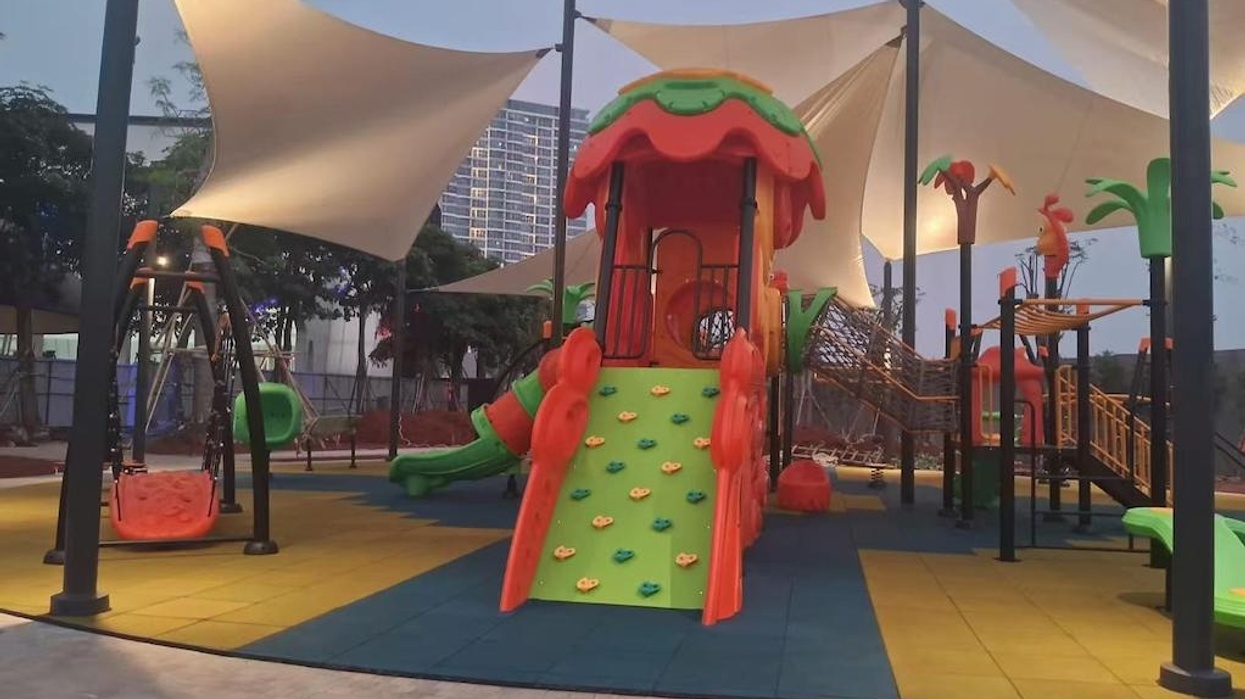 Colorful playground in Jakarta by Dream Garden, with climbing structures and swings under canopy covers.