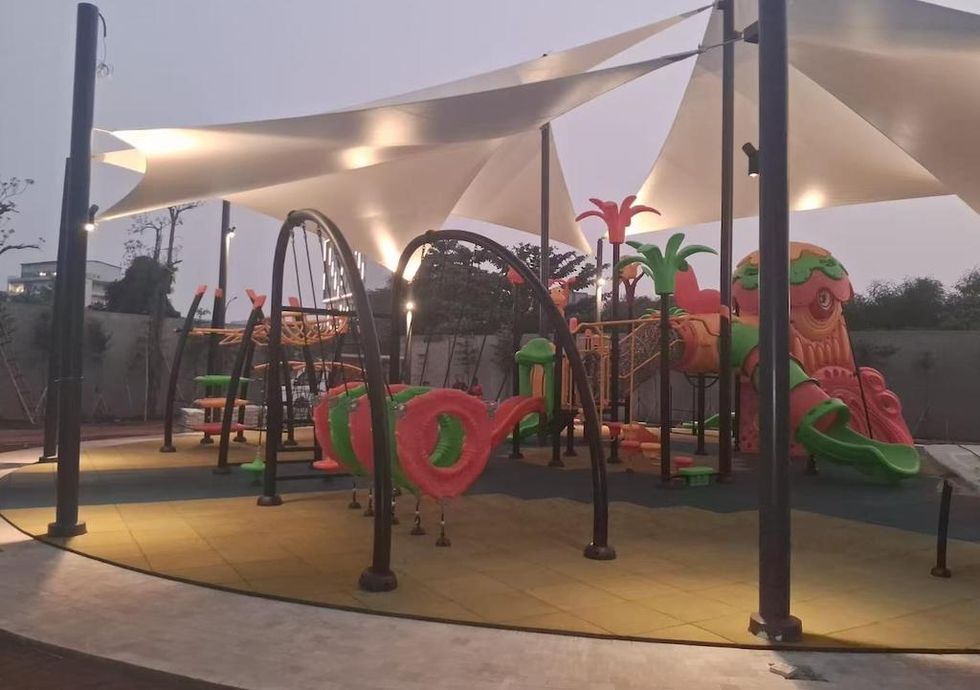 Colorful playground in Jakarta by Dream Garden, with slides and climbing structures under illuminated canopy at dusk.