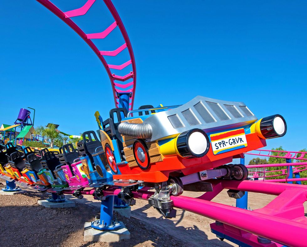Colorful roller coaster car on vibrant pink track under clear blue sky.