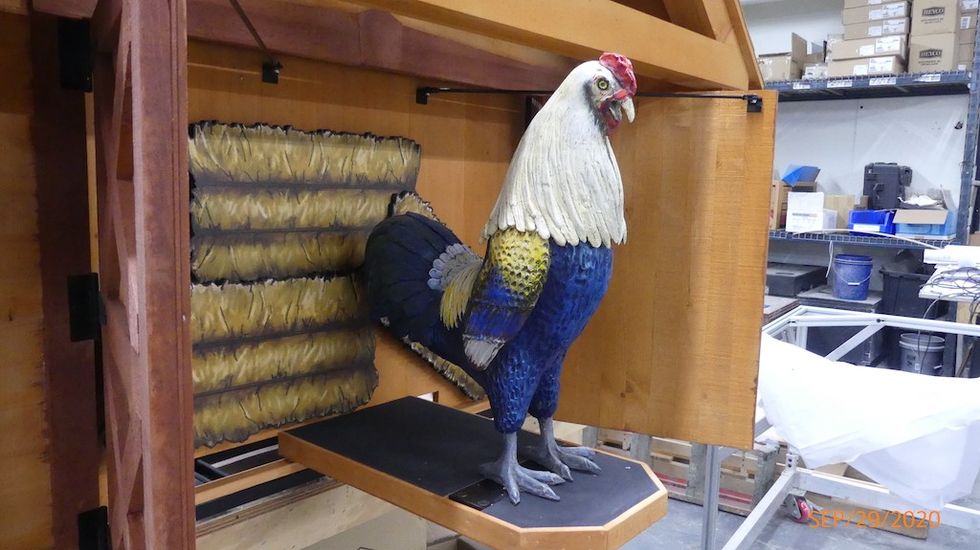 Colorful rooster statue inside a wooden display case, surrounded by shelves.