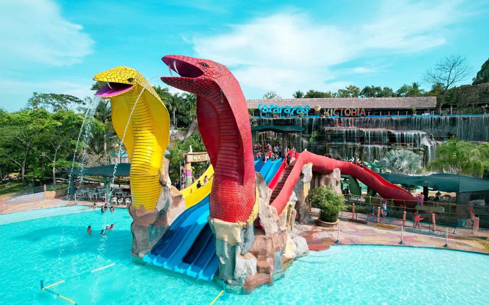 Colorful snake water slides at an outdoor water park called Hacienda Napoles Theme Park, with people swimming