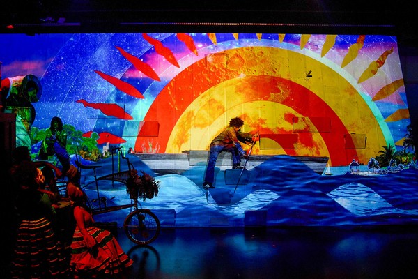 Colorful stage projection with sun, ocean waves, and red fish swimming.
