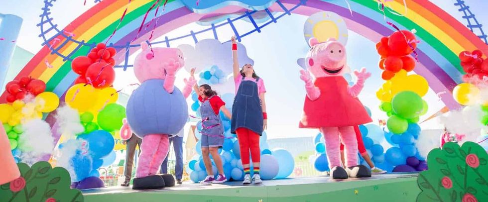 Colorful stage with rainbow arch and costumed characters at a lively outdoor event.