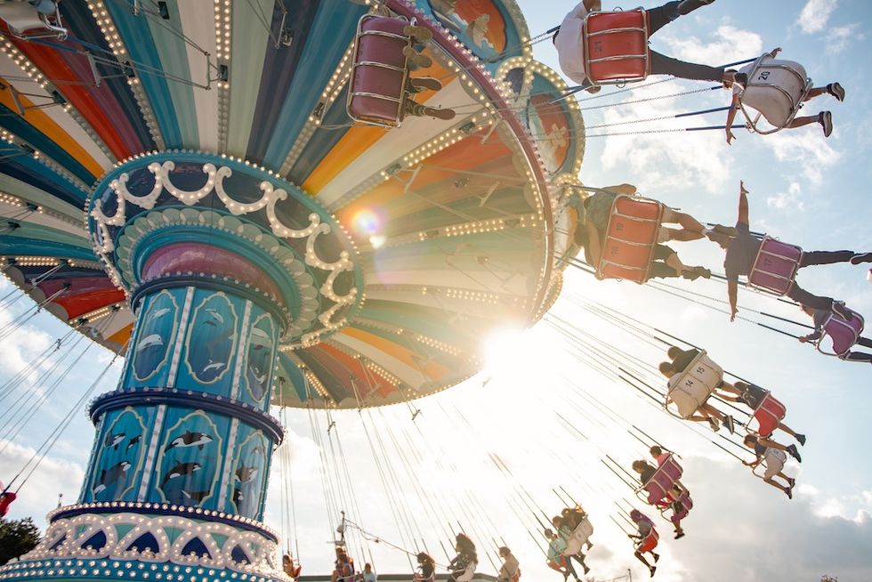 Colorful swing ride with people enjoying the sunny day; bright lights and blue sky.