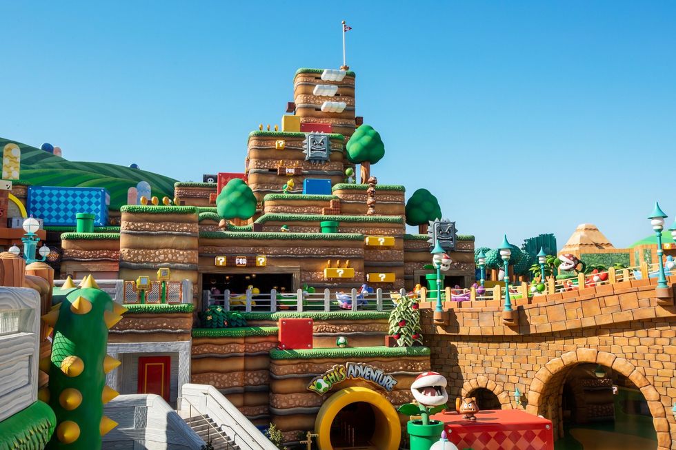 Colorful theme park area called Super Nintendo World with blocky hills, trees, and characters in a fun, fantasy setting.