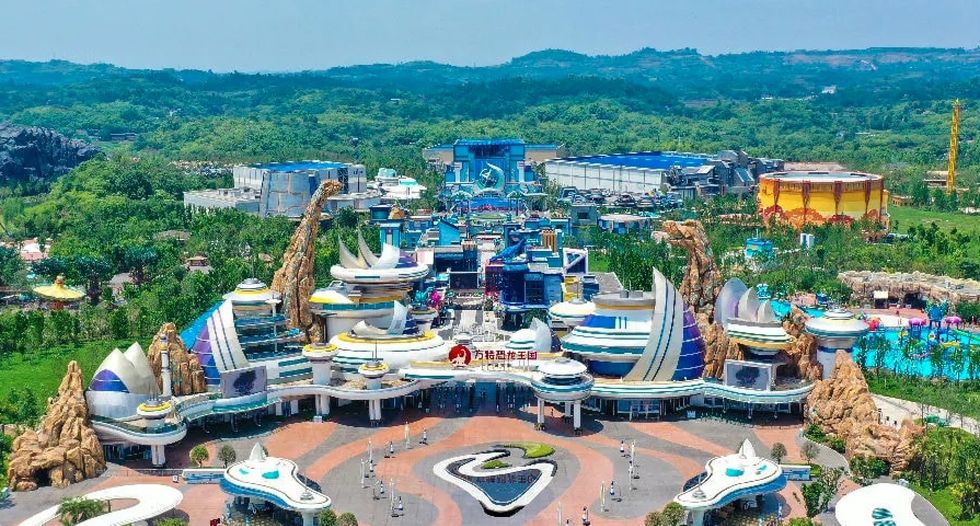 Colorful theme park called Fantawild Dino Kingdom with futuristic buildings and lush green surroundings.