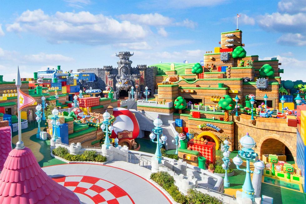 Colorful theme park called Super Nintendo World with Mario-inspired structures and Bowser's dark castle under blue skies.