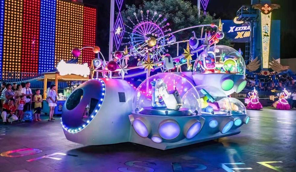Colorful theme park parade with a futuristic float, glowing in vibrant lights.