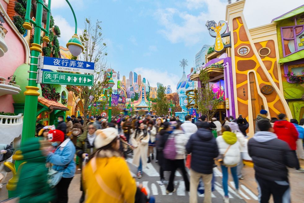 Colorful theme park street at Shanghai Disneyland bustling with people in winter clothing.