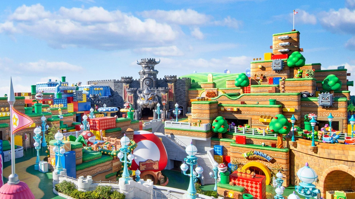 Colorful theme park with castle, hills, and whimsical structures under a blue sky.