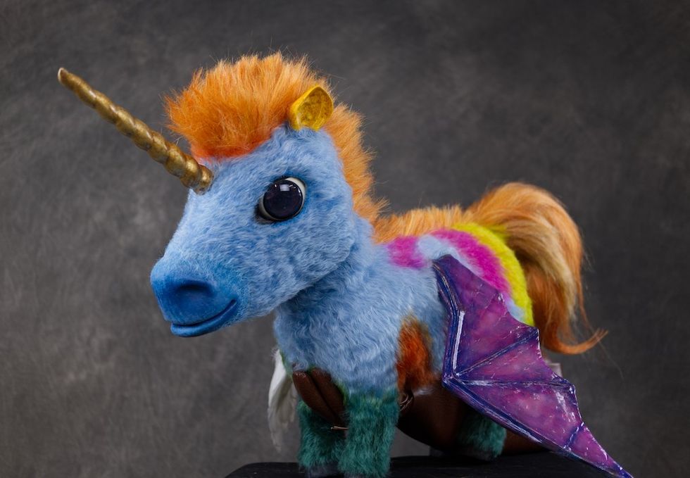 Colorful toy unicorn with wings, blue fur, and golden horn on a dark background.