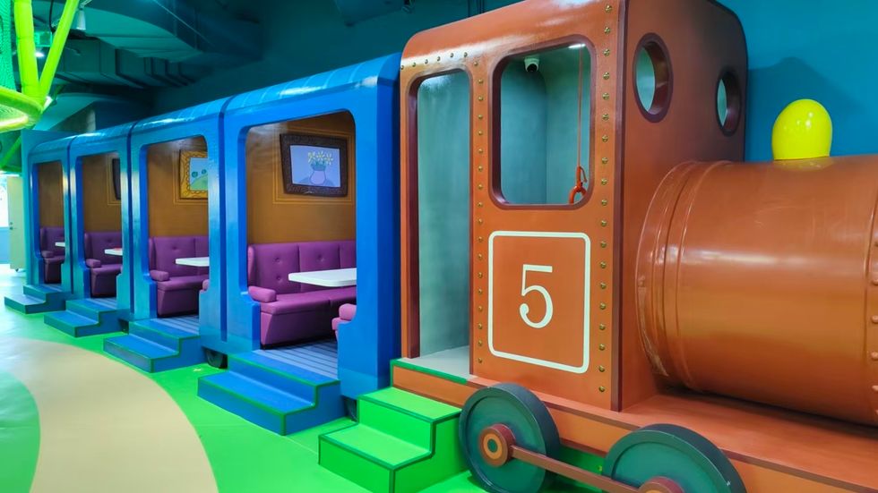 Colorful train-themed seating with booths inside blue train cars and a red engine.