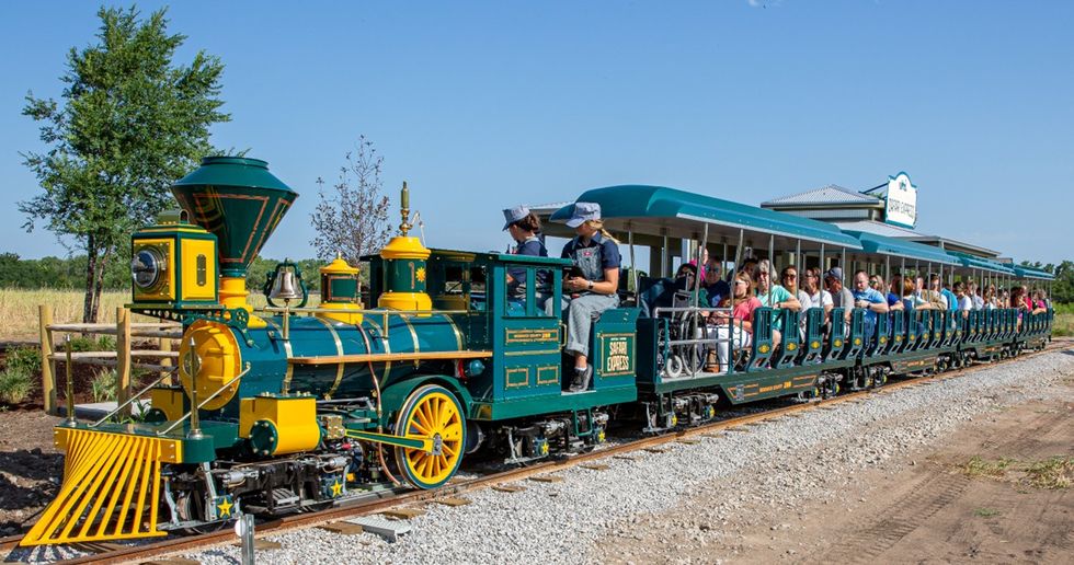 Colorful train with passengers traveling through a natural setting on a sunny day.