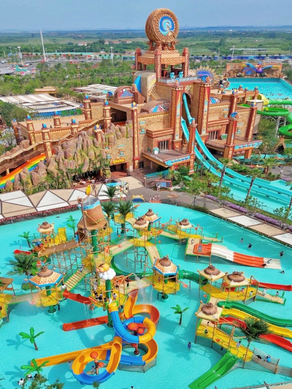 Colorful water park at Xiaogan Fantawild Resort with slides, pools, and a large central structure under a clear sky.