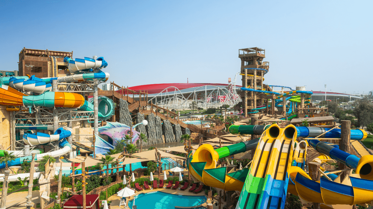 Colorful water park called Yas Waterworld with various slides and a pool under a clear blue sky.