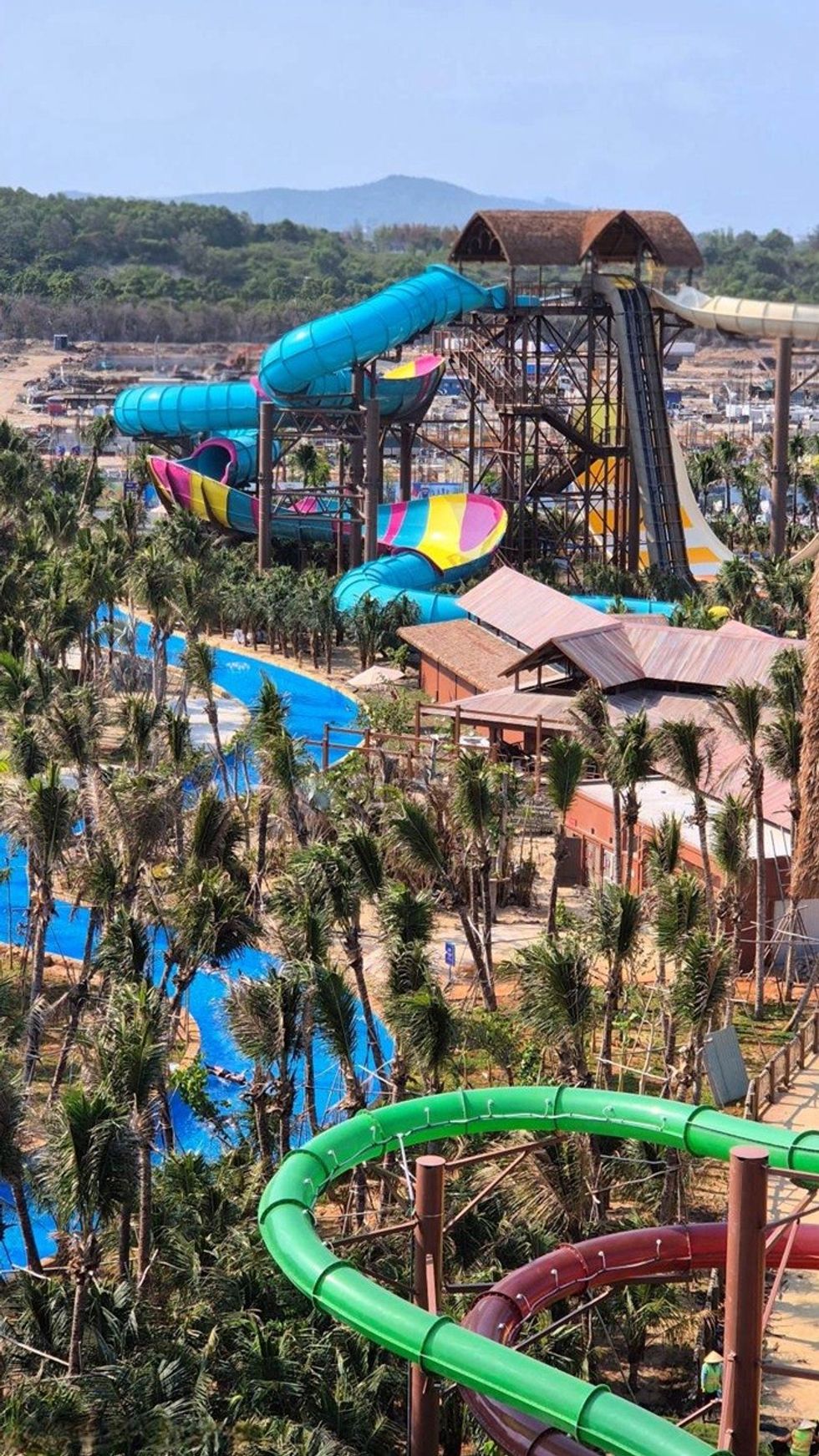 Colorful water park slides surrounded by trees on a sunny day.