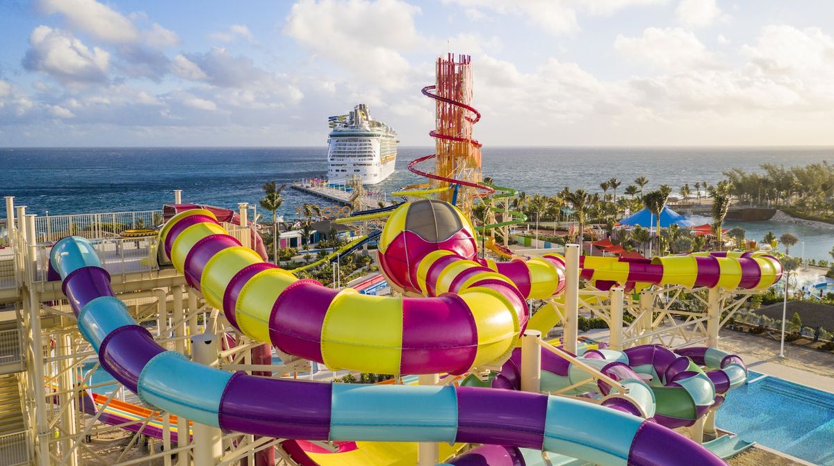 Colorful water park slides with ocean and cruise ship in the background.
