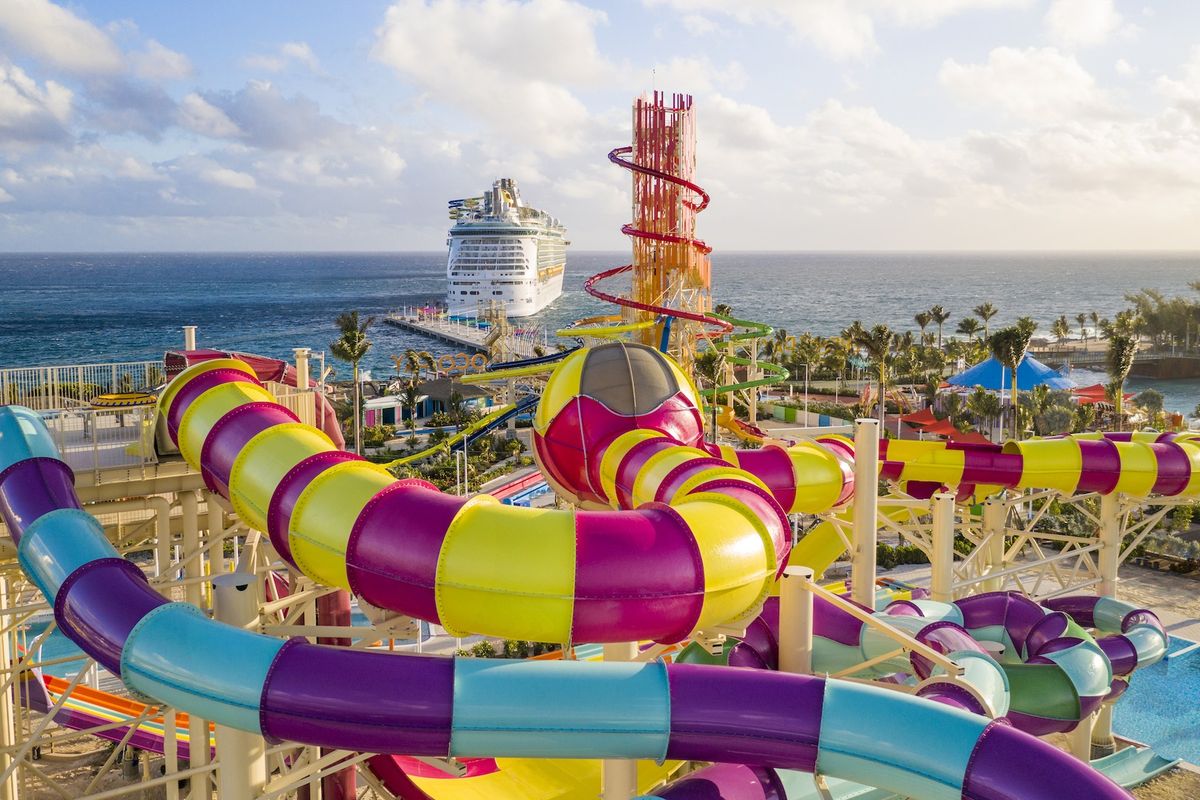 Colorful water park slides with ocean and cruise ship in the background.