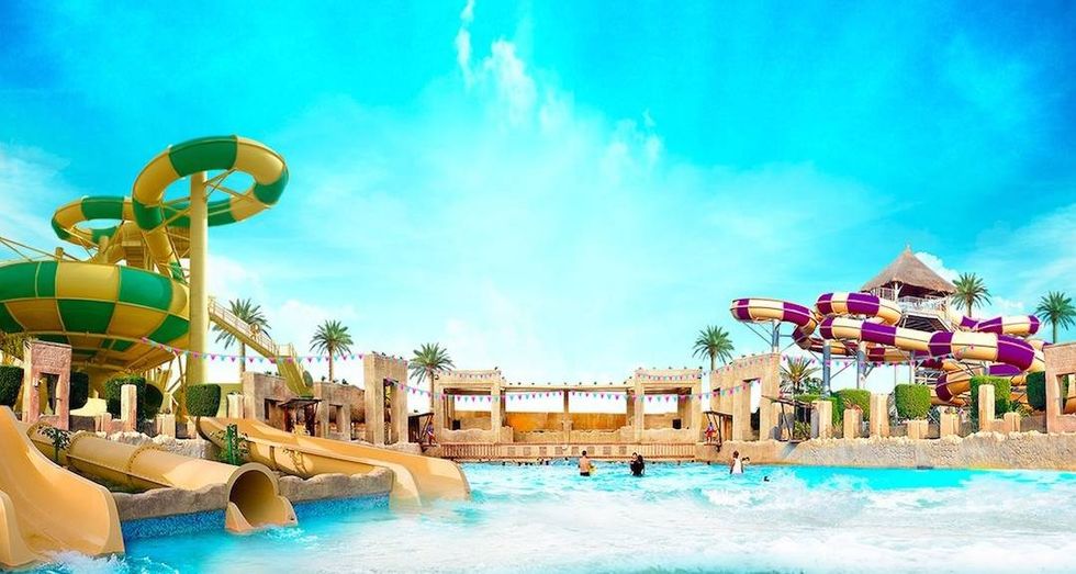 Colorful water park with slides, palm trees, and a wave pool under a bright blue sky at Lost Paradise of Dilmun
