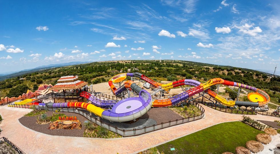 Colorful water slide park with vibrant tubes and lush landscape under a blue sky.