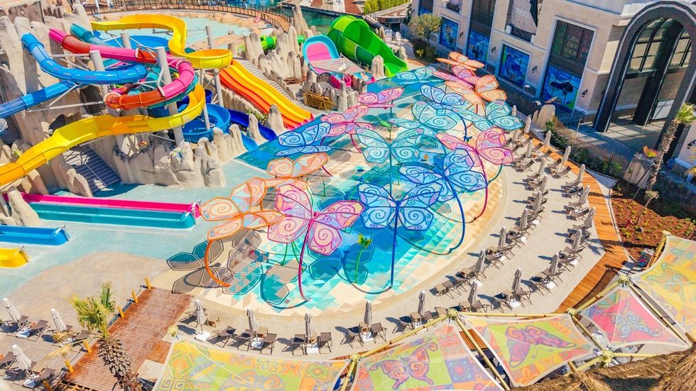 Colorful waterpark with slides and butterfly-shaped shades over a pool area.