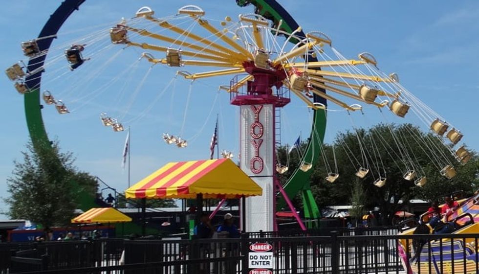 Colorful Yo-Yo swing ride with chairs spinning, set against a clear blue sky.