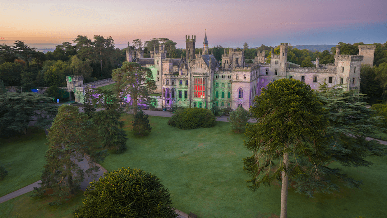 Colorfully lit, historic castle surrounded by trees at sunset.