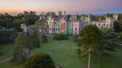 Colorfully lit, historic castle surrounded by trees at sunset.