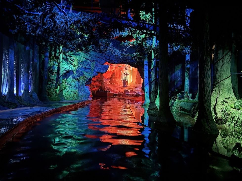 Colorfully lit tunnel with a ship silhouette and reflections on the water.