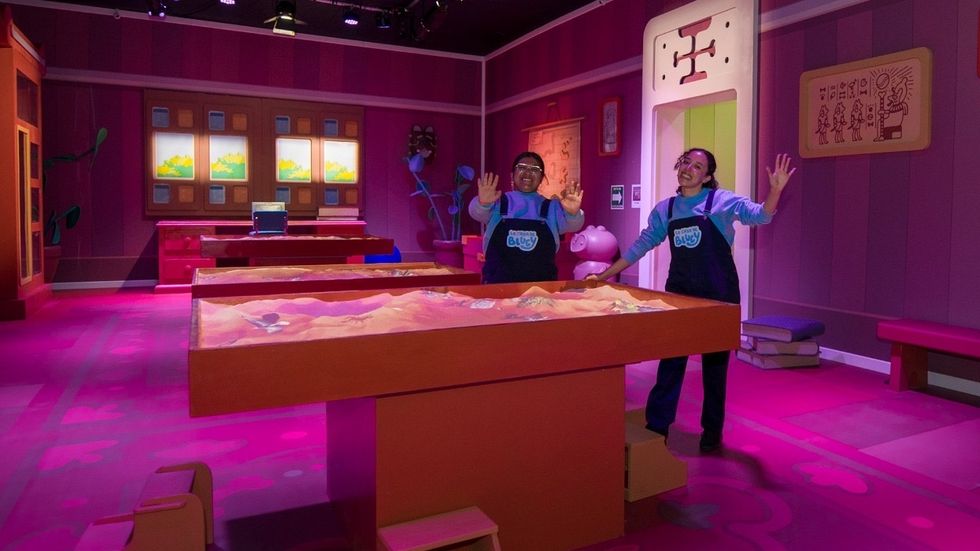 Colourful interactive exhibit with two smiling guides in a vibrant room.