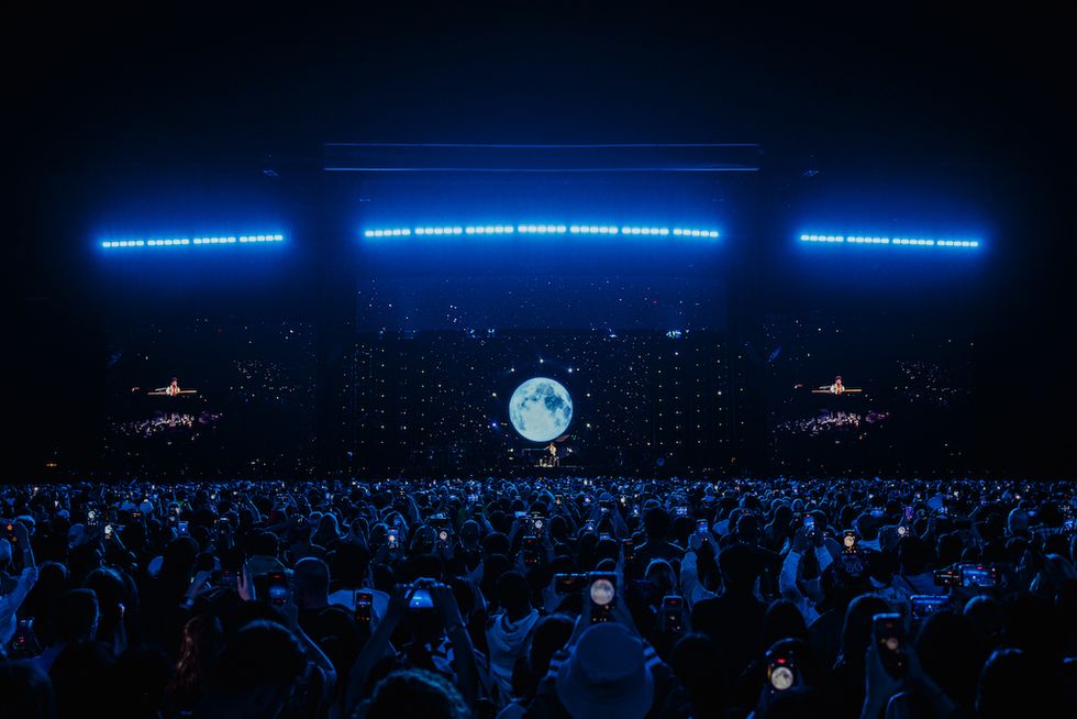 Concert audience under blue lights with a large moon display on stage.