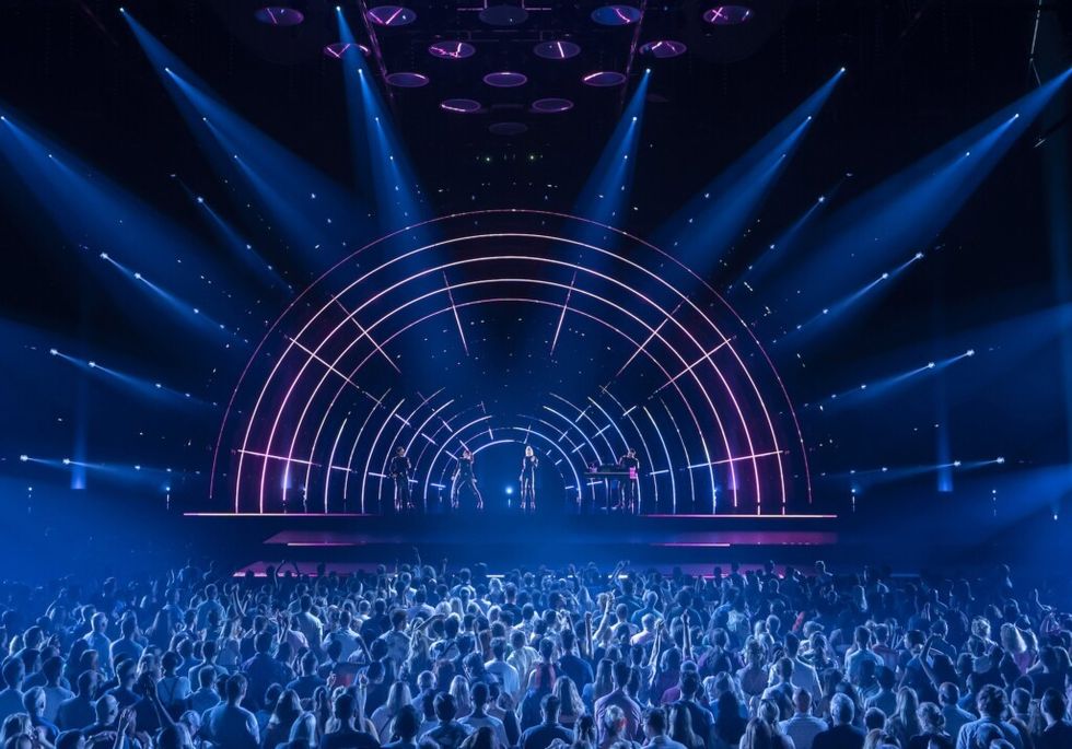 Concert stage with arched lights, performers, and a large audience.