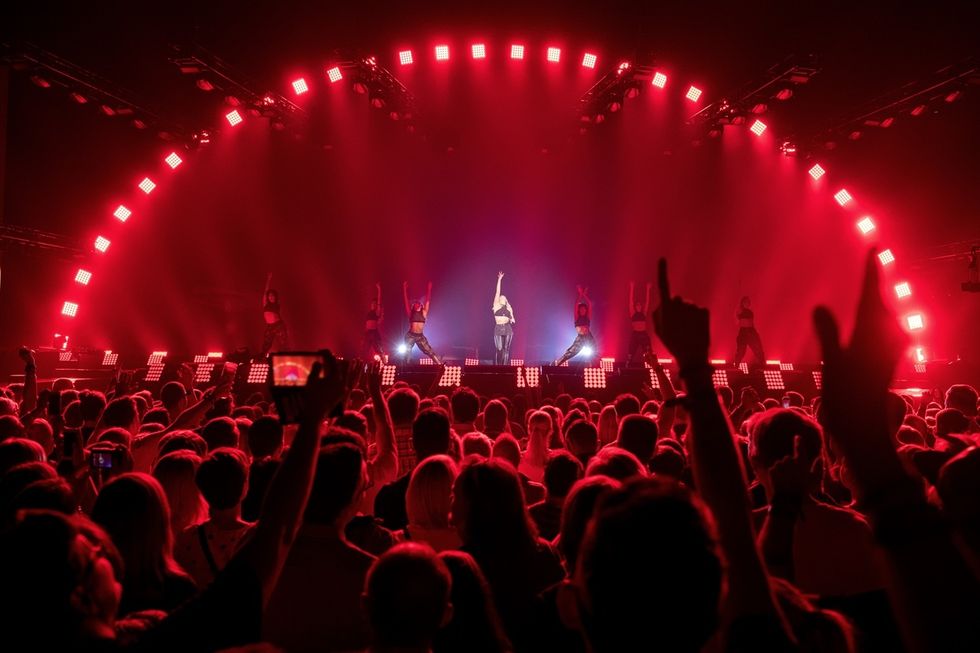 Concert with red lighting, dancers on stage, and cheering crowd at a Cirque du Soleil performance.