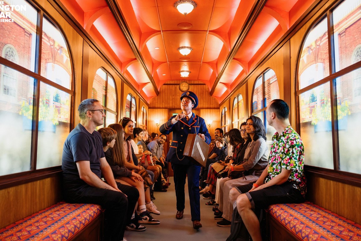 Conductor with suitcase walks down train aisle as passengers watch attentively.