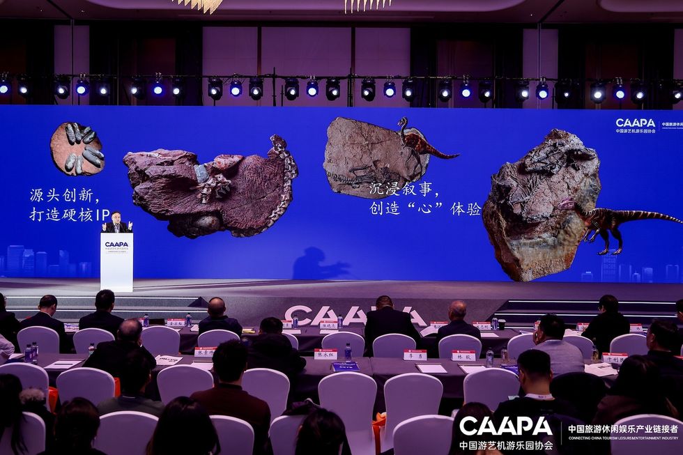 Conference stage with speaker, dinosaur fossils, and blue backdrop.
