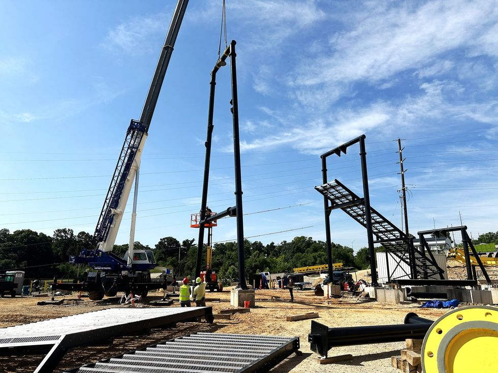 Construction site at Oasis at Lake of the Ozarks with crane lifting a steel structure, workers and equipment around.