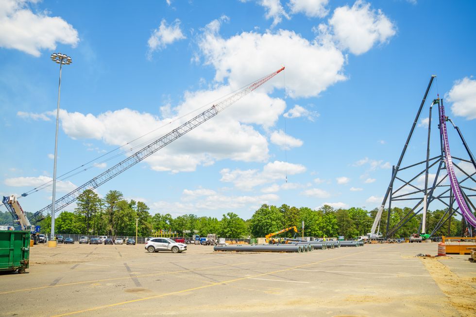 Construction site with a crane at Six Flags Great Adventure and large metal roller coaster structure under a bright blue sky.