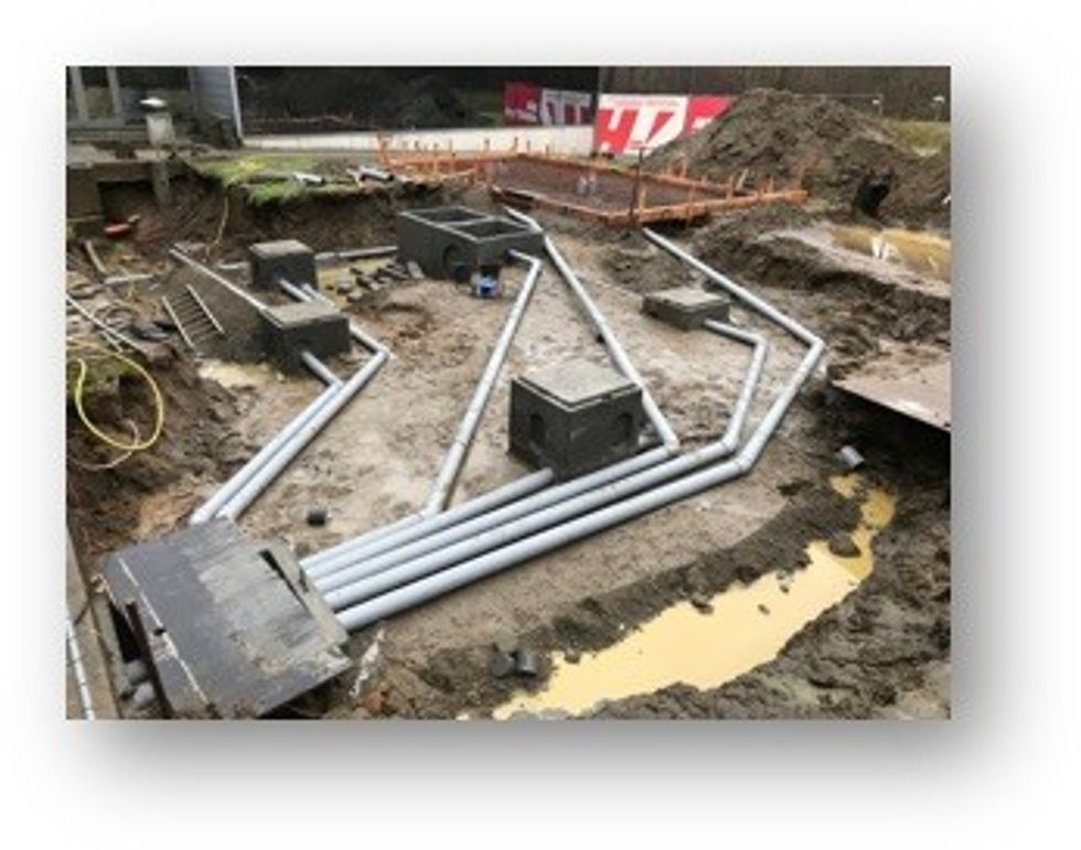 Construction site with exposed pipes and concrete enclosures in muddy ground.
