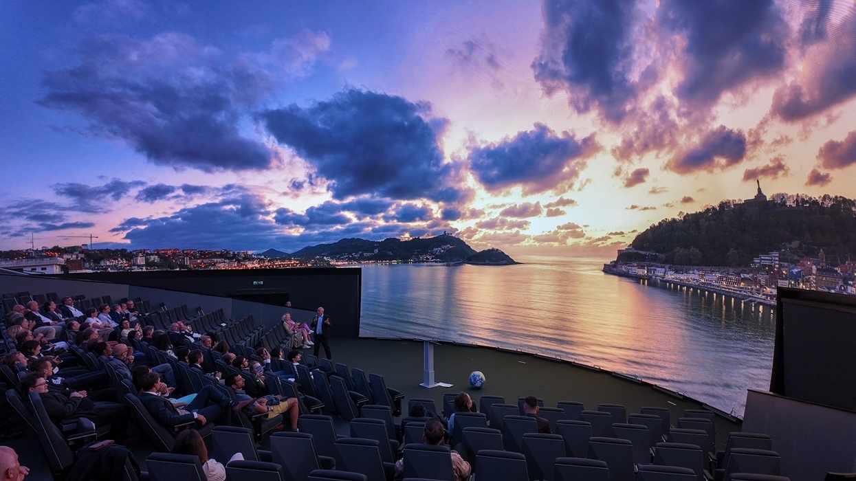 Cosm dome theatre showing an ocean view under a colourful sunset sky, audience seated in rows.