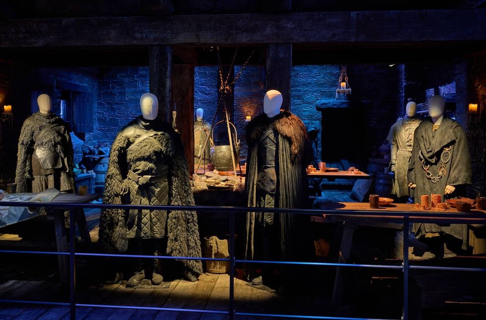 Costumes displayed on mannequins in a medieval-themed, dimly lit setting.