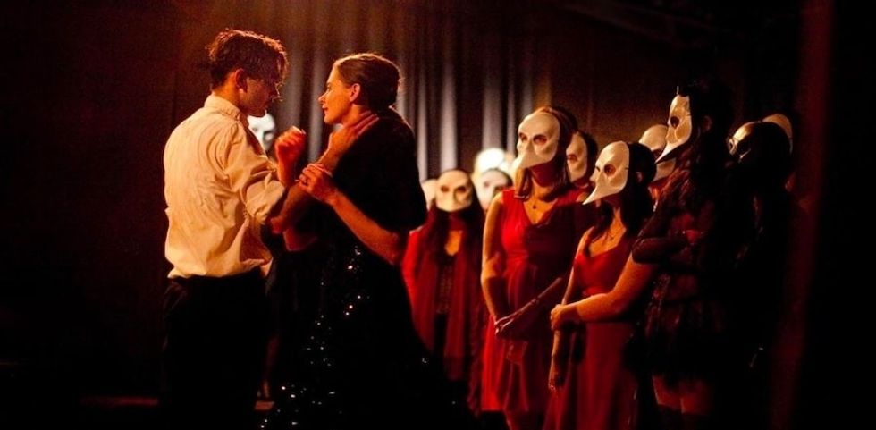 Couple dancing in dim light, watched by masked onlookers in red attire in Sleep No More from Punchdrunk