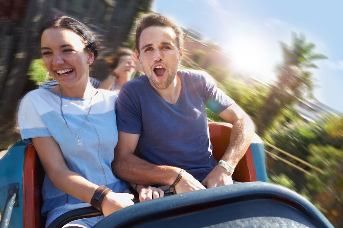 Couple enjoying a thrilling roller coaster ride on a sunny day.