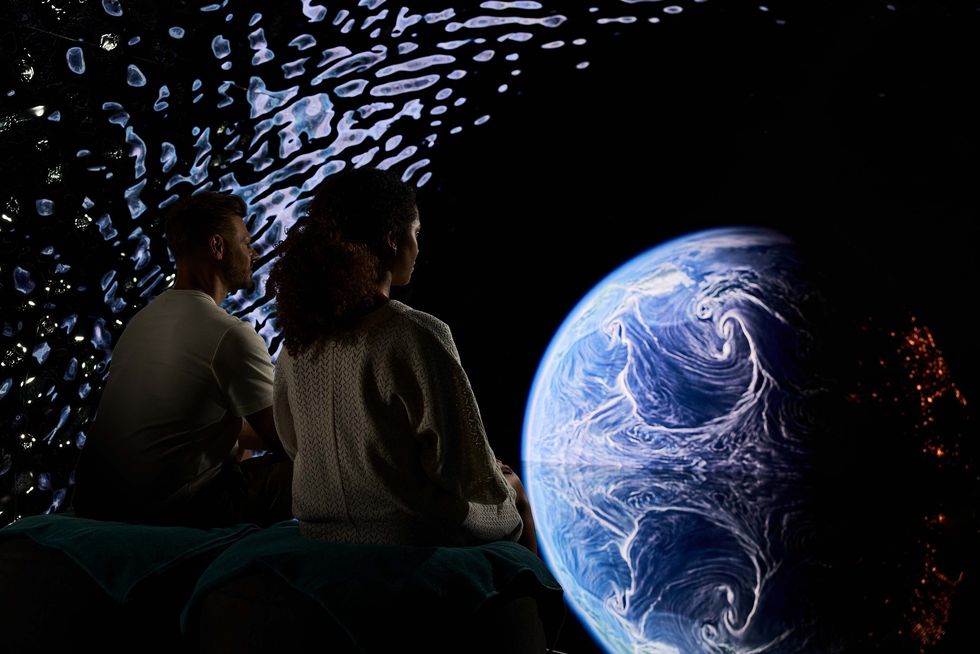 Couple gazes at a cosmic, swirling Earth projection with abstract patterns in the background.