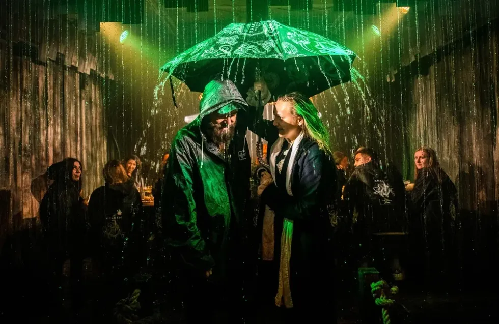 Couple in rain with umbrella, dimly lit green-hued bar setting, others in background.