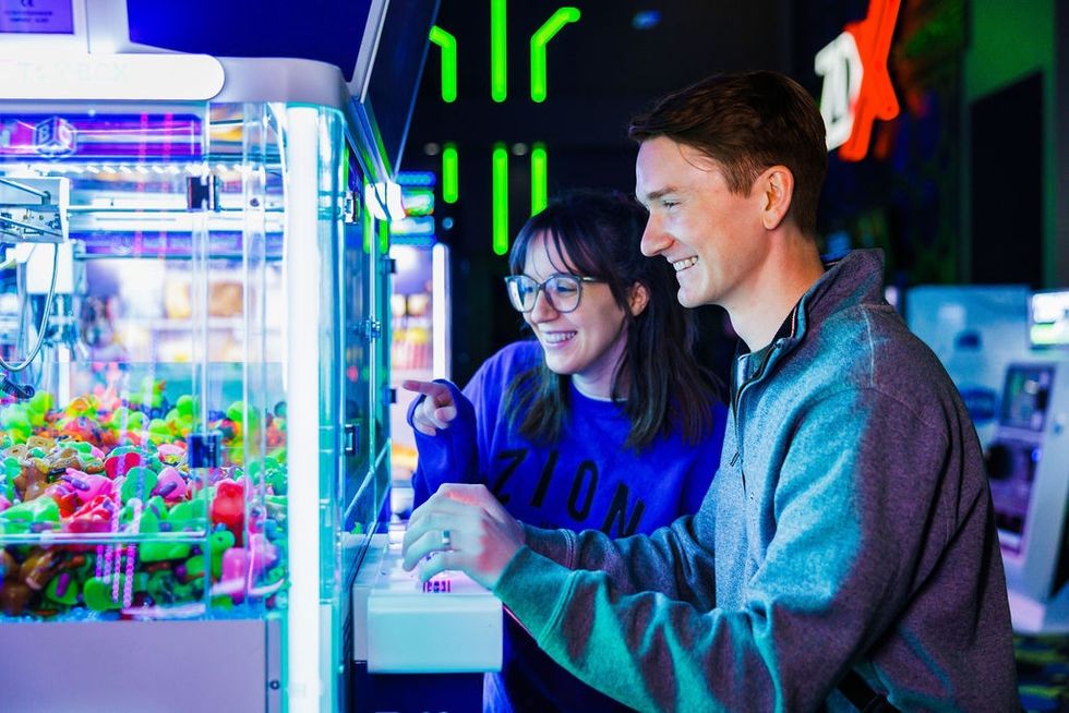 Couple playing a claw machine in a neon-lit arcade, smiling and enjoying the game.