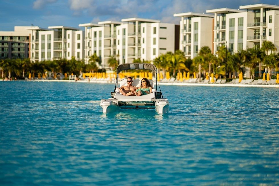 Couple relaxing on a motorised chaise lounge near modern beachside apartments.